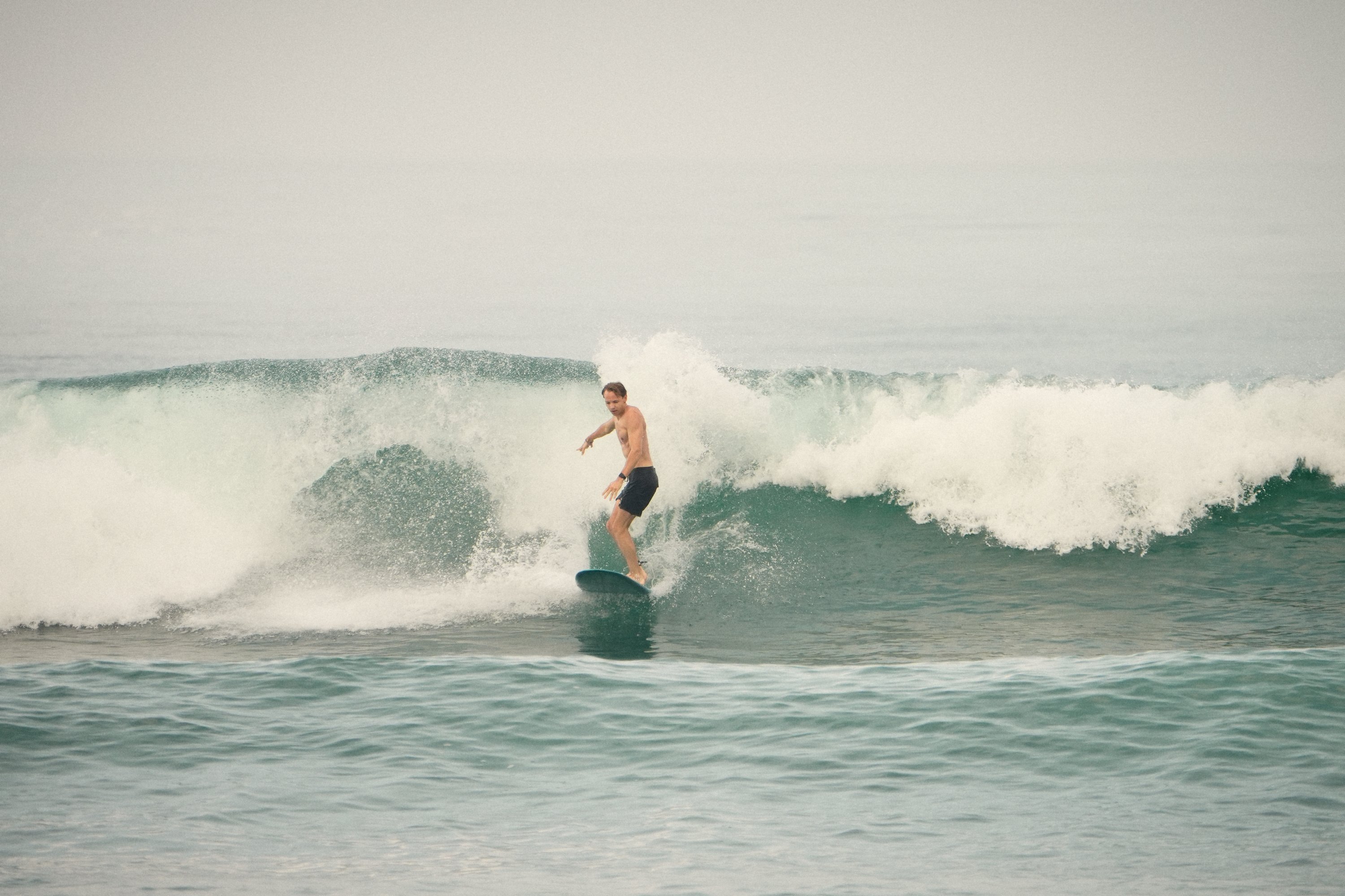 The biggest wave of the morning curling behind a small surfer